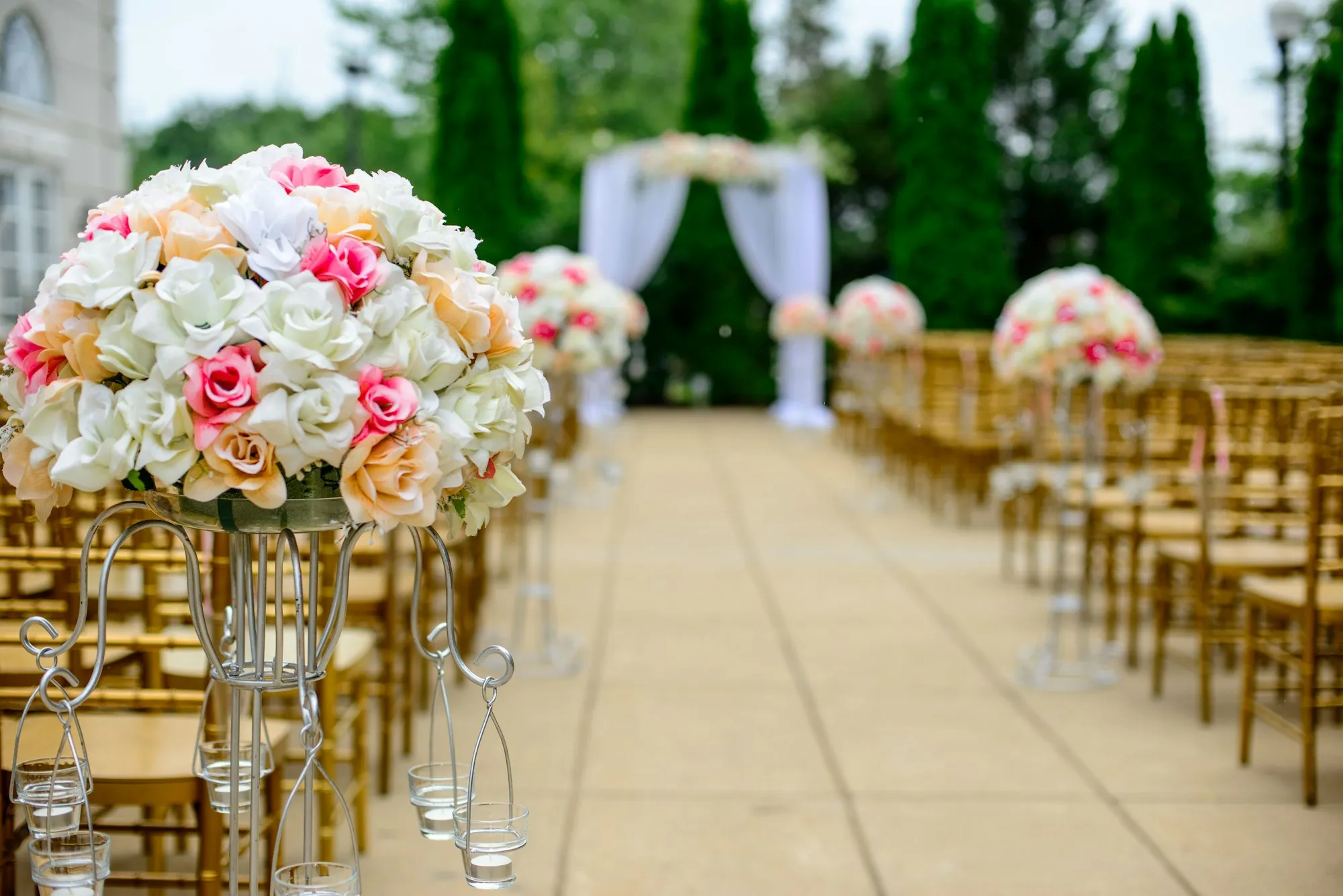 An outdoor ceremony aisle lined with roses, leading to a draped arch