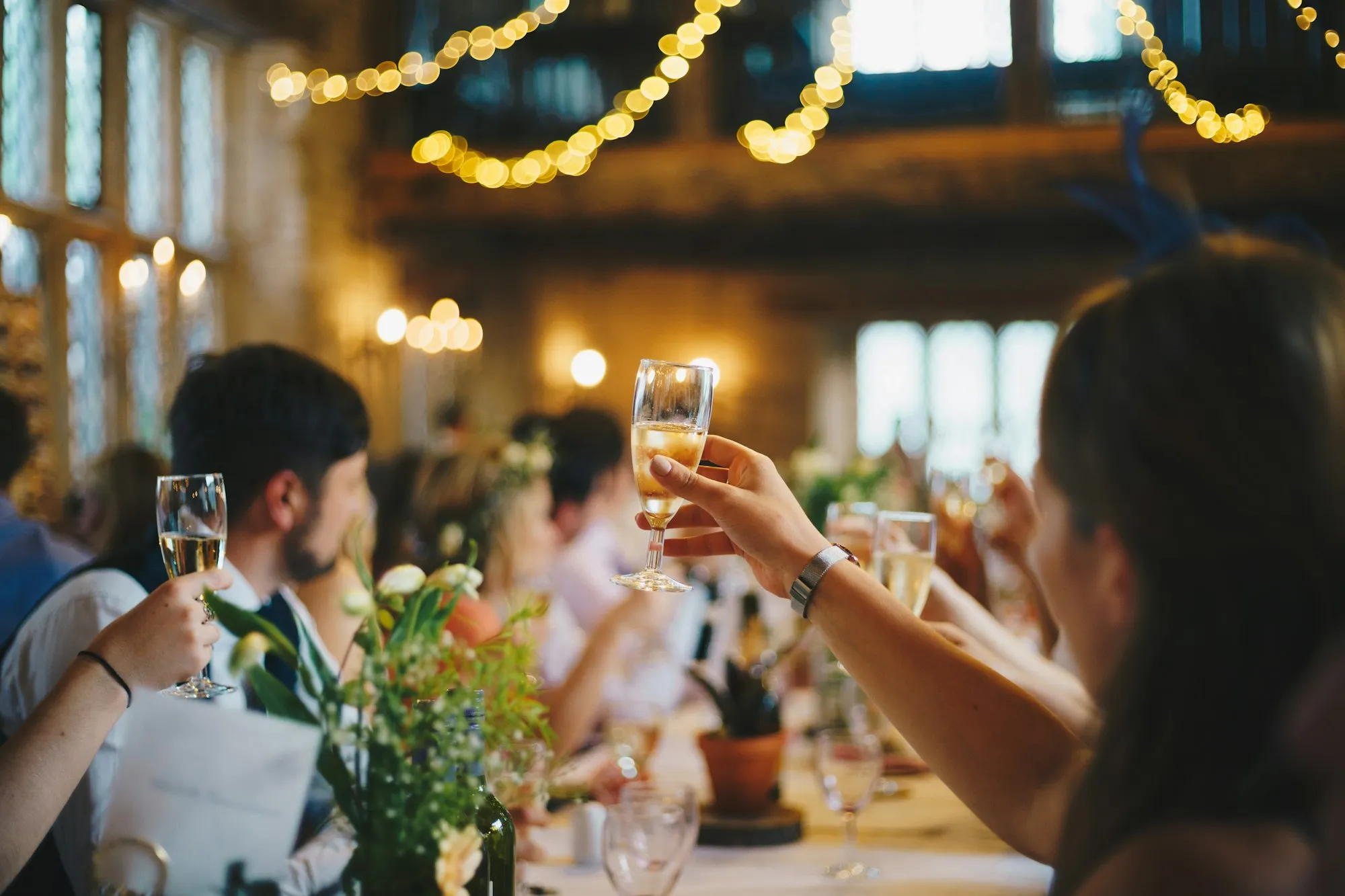 A guest raising a glass of champagne at a long table under string lights